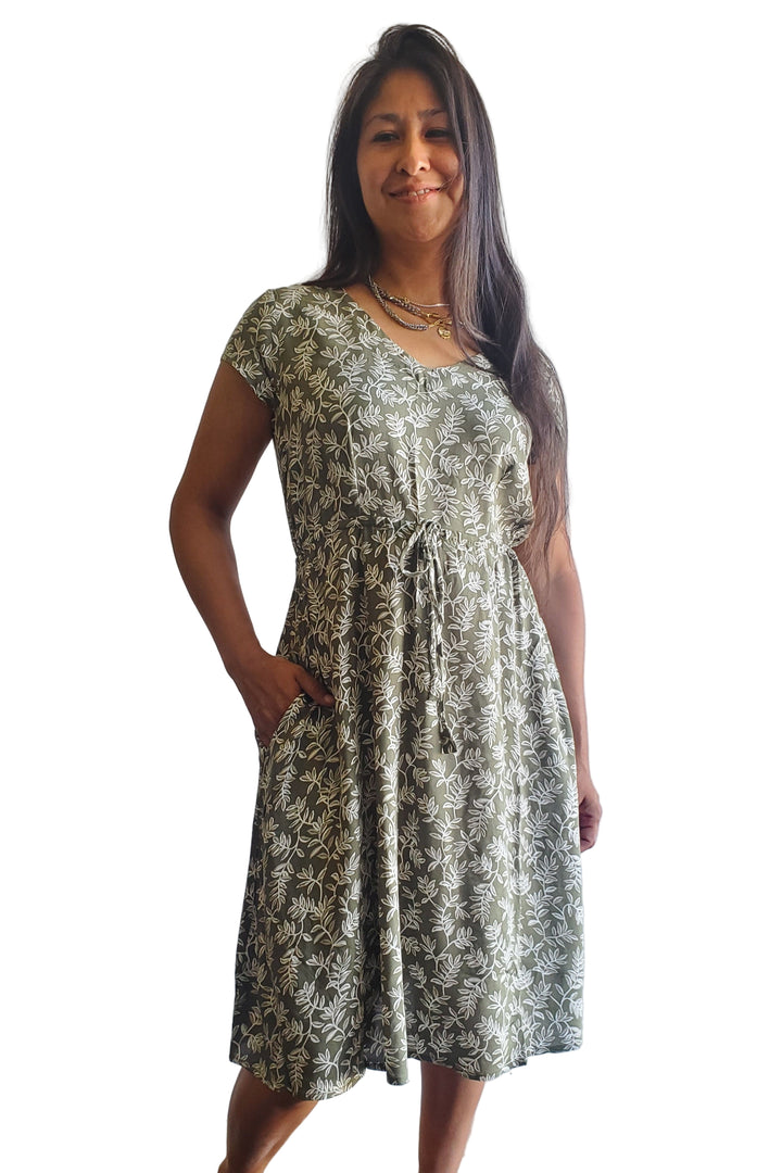 Woman wearing a patterned dress standing against a light blue wall.